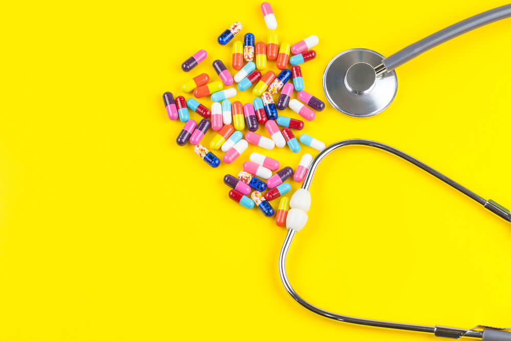 stethoscope and colourful pills on a yellow background